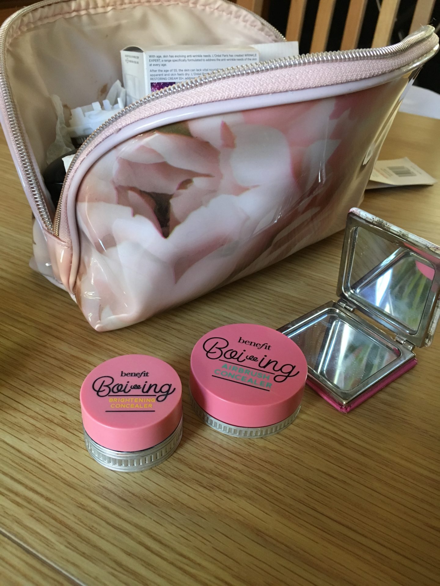 pink flowers make-up bag with benefit brightening and airbrush concealer with hand mirror sitting in front of it 