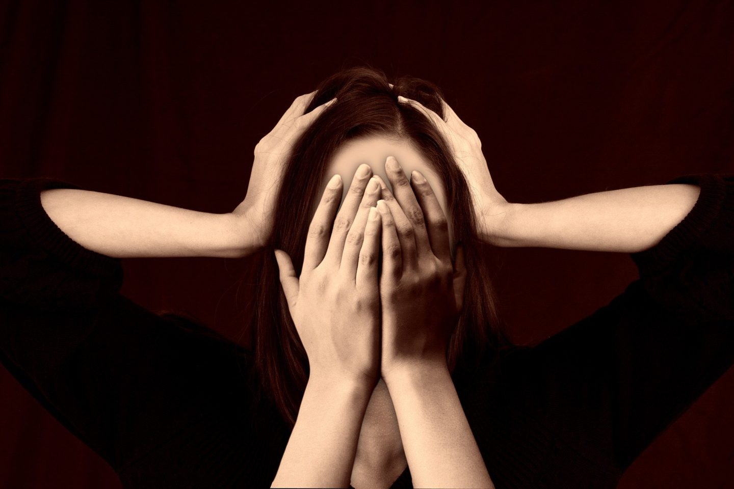 Picture of woman covering her face with both hands, with another pair of hands covering both sides of her head